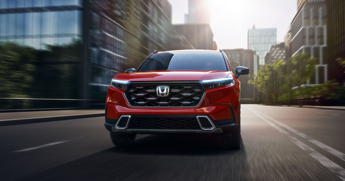2025 Honda CR-V Hybrid Sporting Touring trim in Radiant Red Metallic driving through a city.