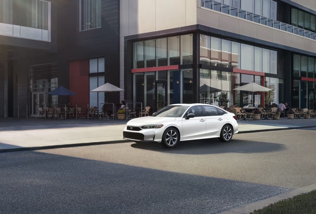 The white new 2025 Honda Civic is shown driving down a beautiful city street. Shop for your new Honda Civic near Atlanta at Stonecrest Honda.