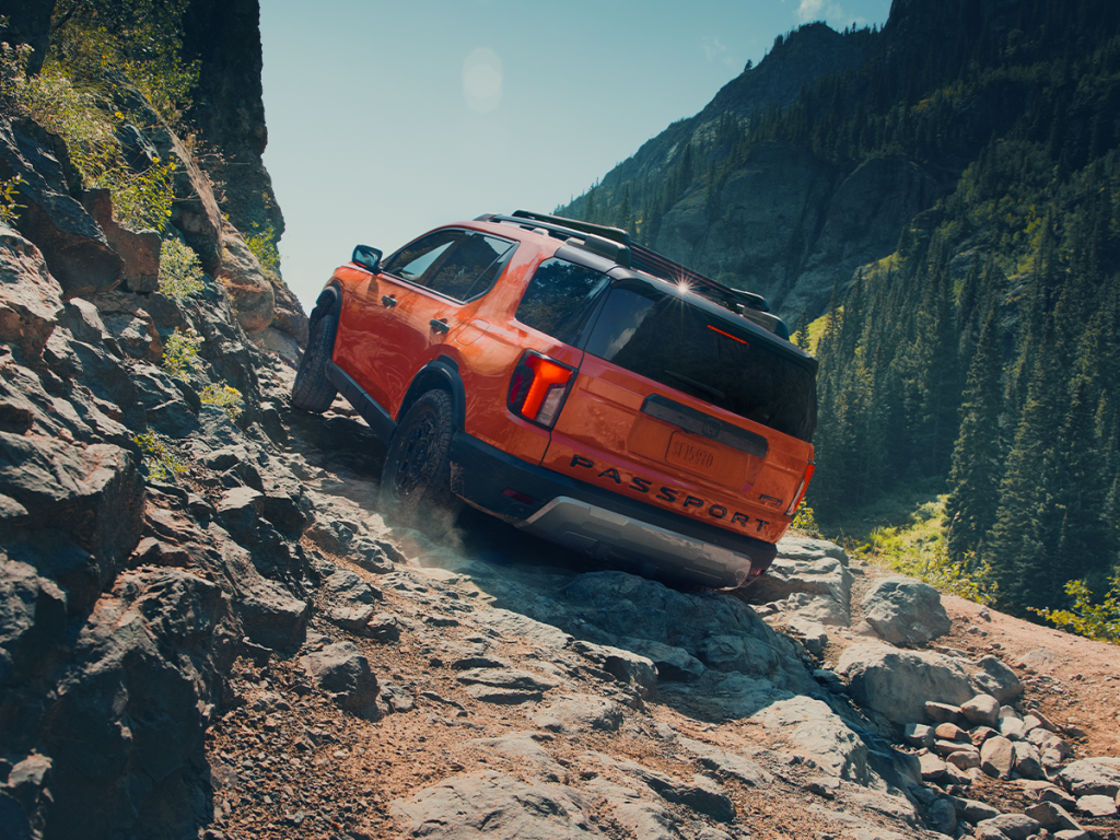 An orange Honda Passport climbs up a rocky mountainside trail.